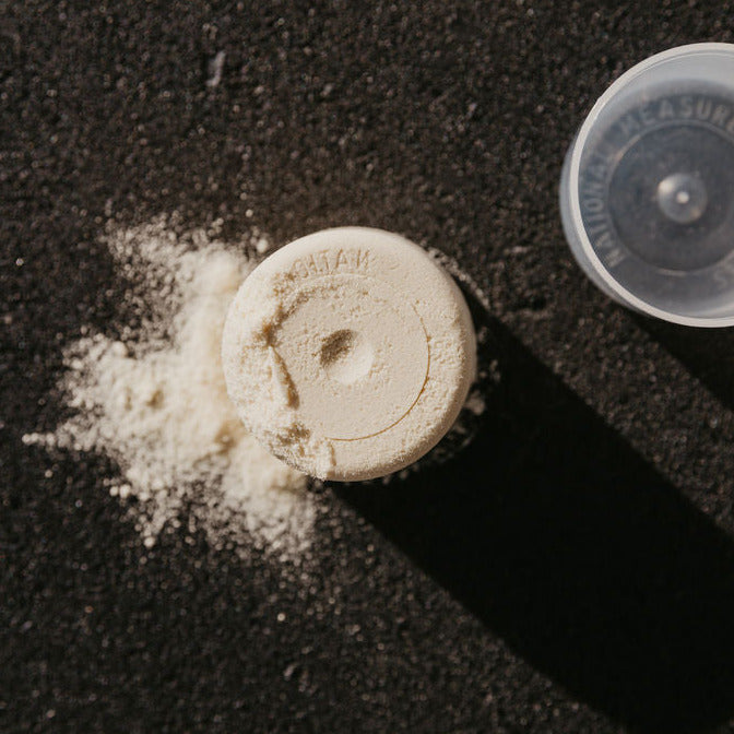 A serving of protein powder next to plastic scoop on black background.