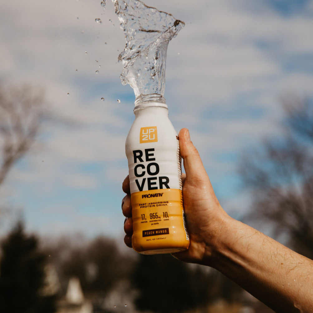 Hand holding a bottle of UP2U recovery drink to the sky, spilling clear liquid.