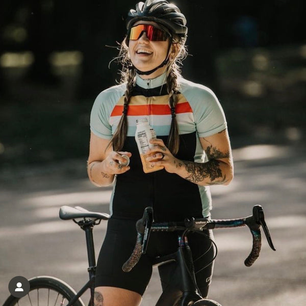 Laughing Female cyclist stands with bike taking drink of UP2U recovery drinking