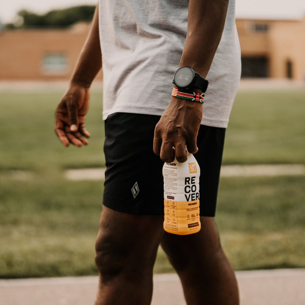 Runner walking on track holding bottle of UP2U recovery drink.