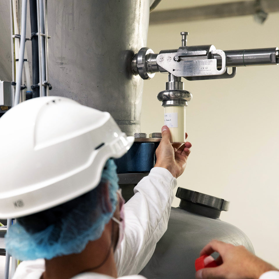 Food scientist in a hard hat and white coat collecting a sample from a machine.